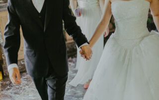 Woman wearing white wedding gown holding hands with man while walking