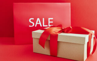 Cardboard box with red ribbon beside a sale sign