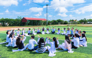 People sitting on green lawn grass while doing hands up at daytime